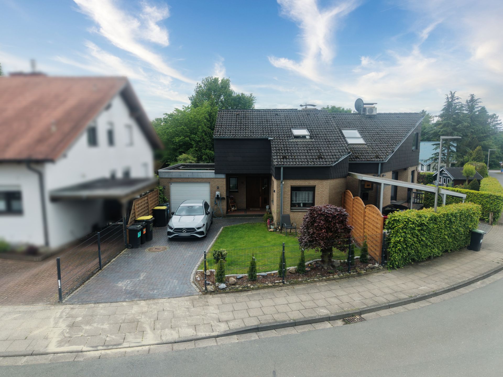 Modernes Einfamilienhaus mit Garten, Einfahrt, Auto und angrenzender Garage an einer ruhigen Straße.