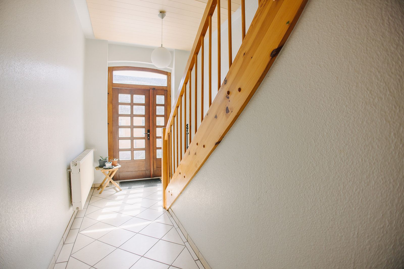 Heller Flur mit Holztür, Holztreppe und kleinem Tisch mit Pflanzen.