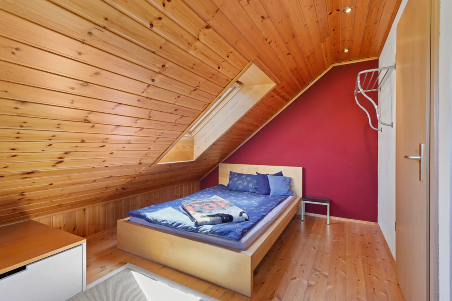 Gemütliches Schlafzimmer mit Holzdecke, Einzelbett und roter Wand unter Dachschräge.
