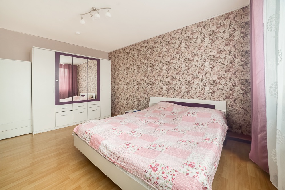Schlafzimmer mit Doppelbett, floraler Tapete und weißem Kleiderschrank mit Spiegeln.
