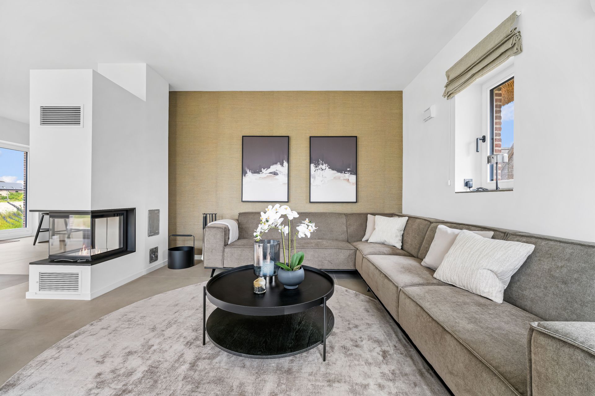 Modernes Wohnzimmer mit Ecksofa, rundem Couchtisch, Kamin und zwei Bildern an der Wand.