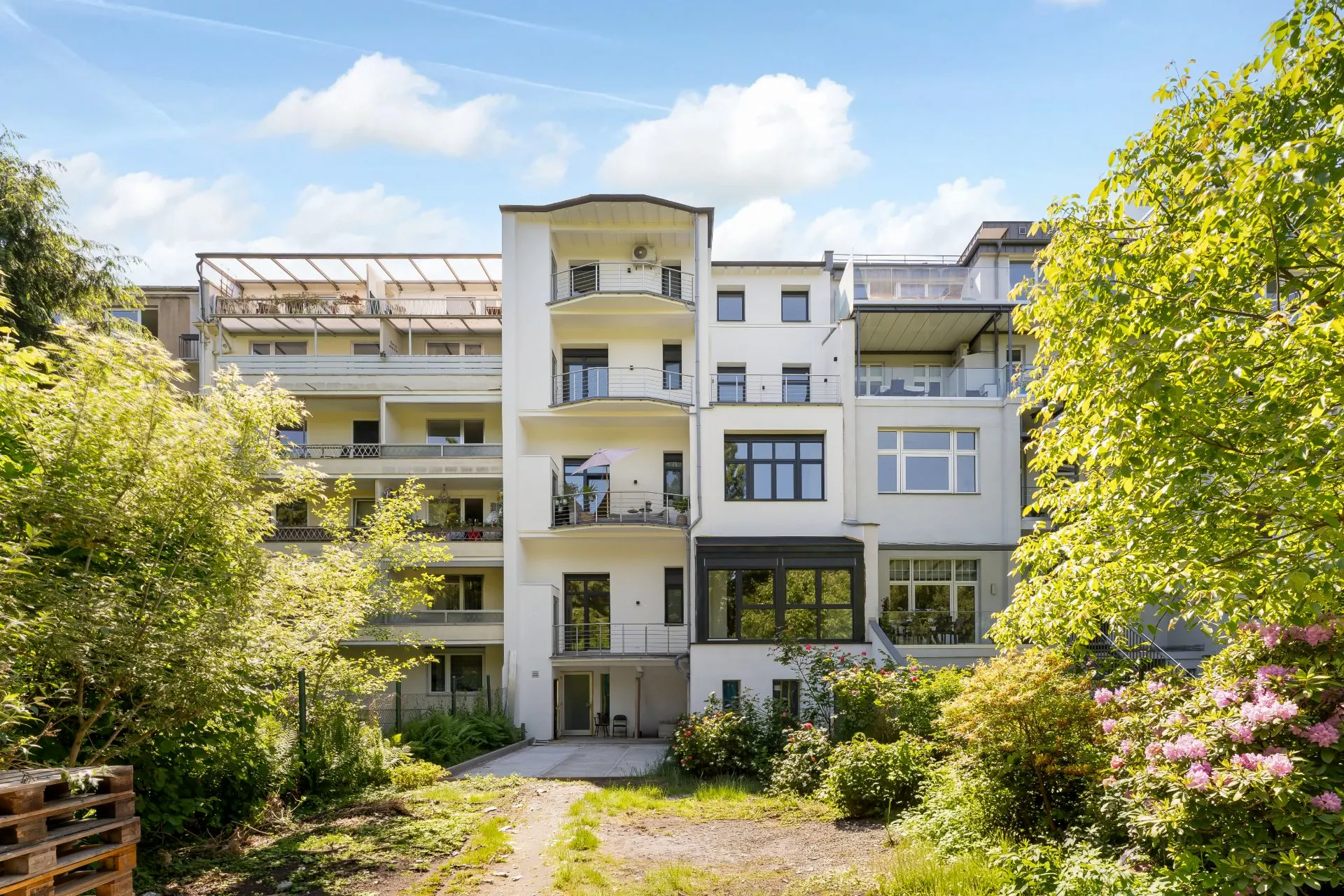 Mehrstöckiges Wohnhaus mit Balkonen und Garten im Vordergrund.