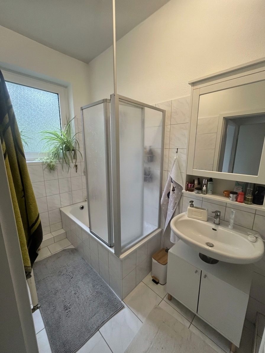 Kleines Badezimmer mit Dusche, Waschbecken, Spiegel und Fenster mit Pflanze.