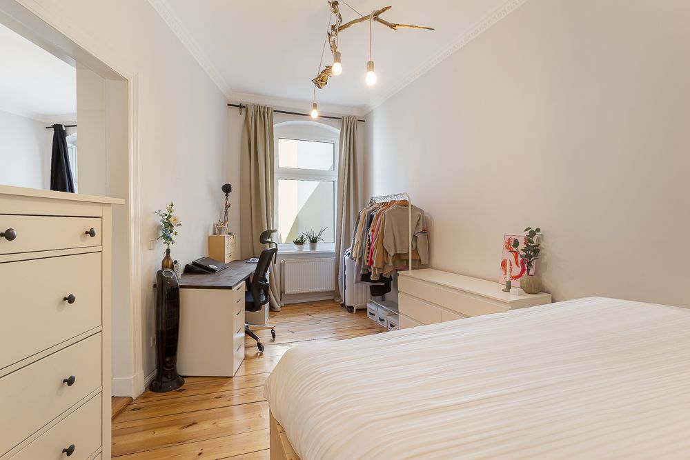 Helles Schlafzimmer mit Bett, Schreibtisch, Kommode, Fenster und Kleiderständer.