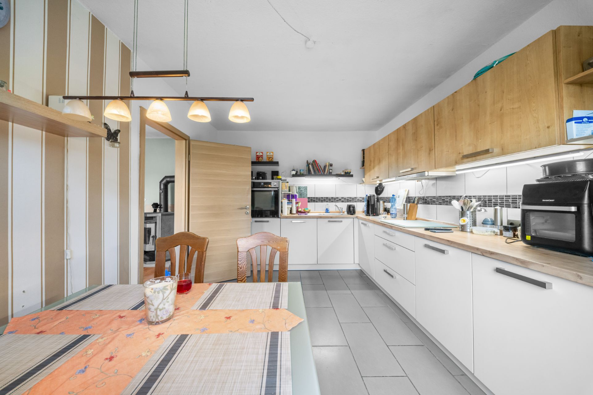Moderne Küche mit Holzmöbeln, Esstisch, Stühlen und Hängelampen, offen zur Tür.