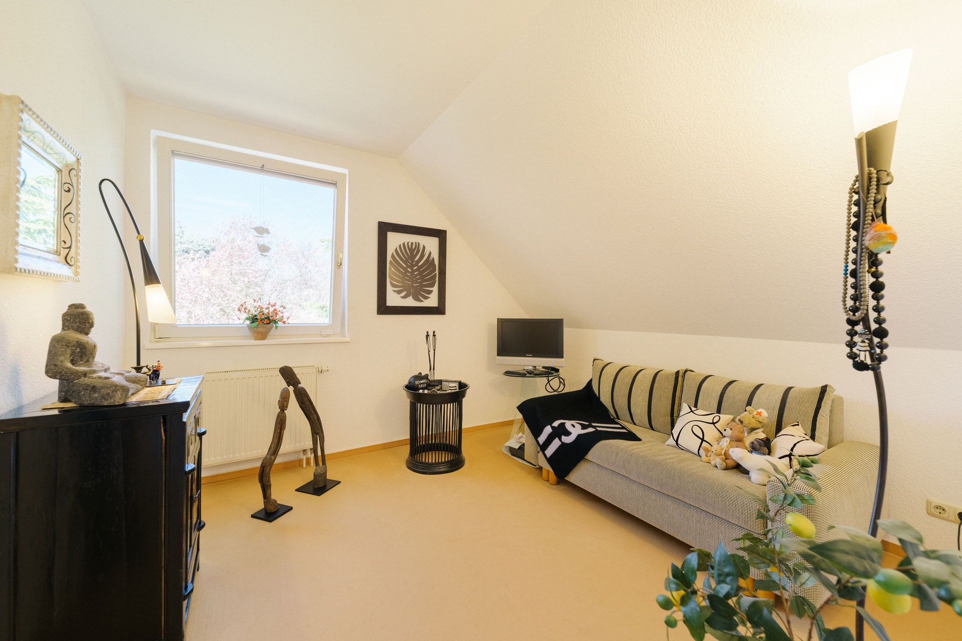 Gemütliches Zimmer mit Sofa, kleinem Fernseher, Dekorationen und großem Fenster unter einer Dachschräge.