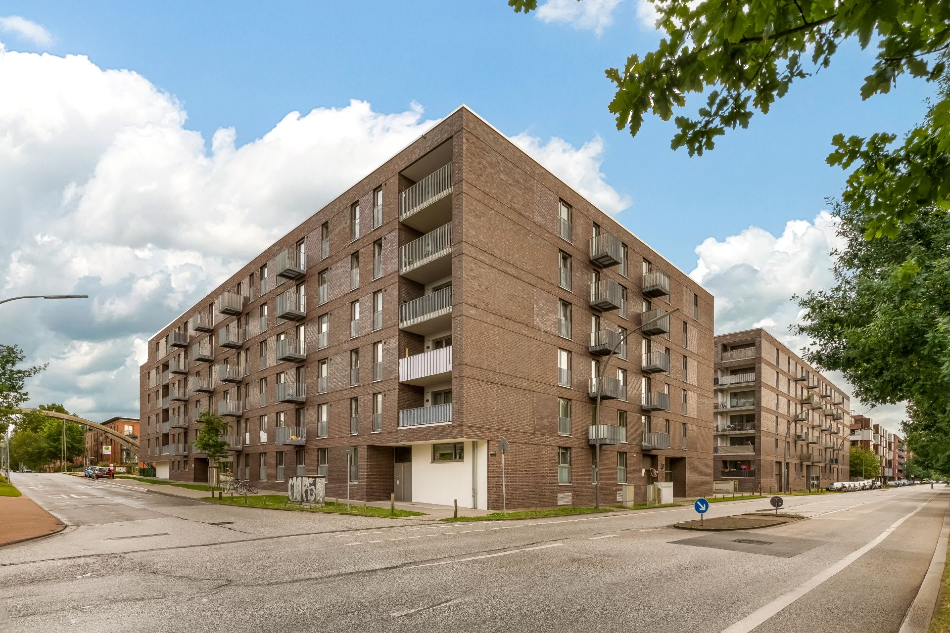 Modernes mehrstöckiges Wohngebäude aus Backstein mit Balkonen an einer Straßenecke.