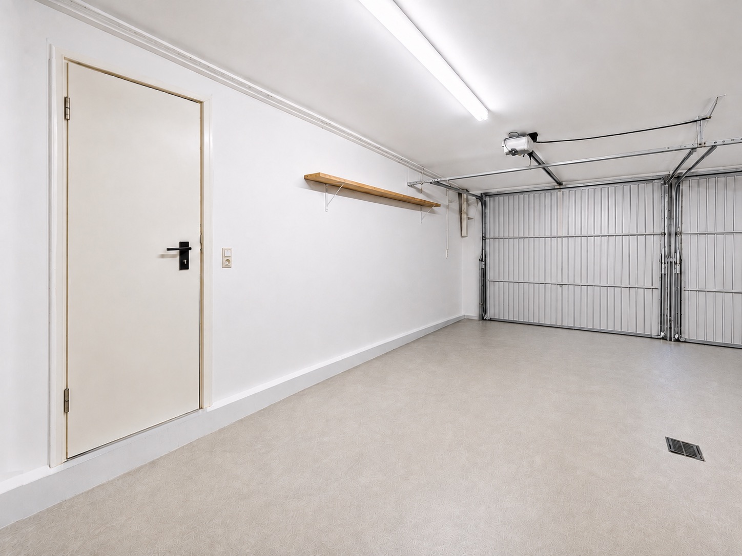 Leere Garage mit weißer Tür, Wandregal und geschlossenem Garagentor.