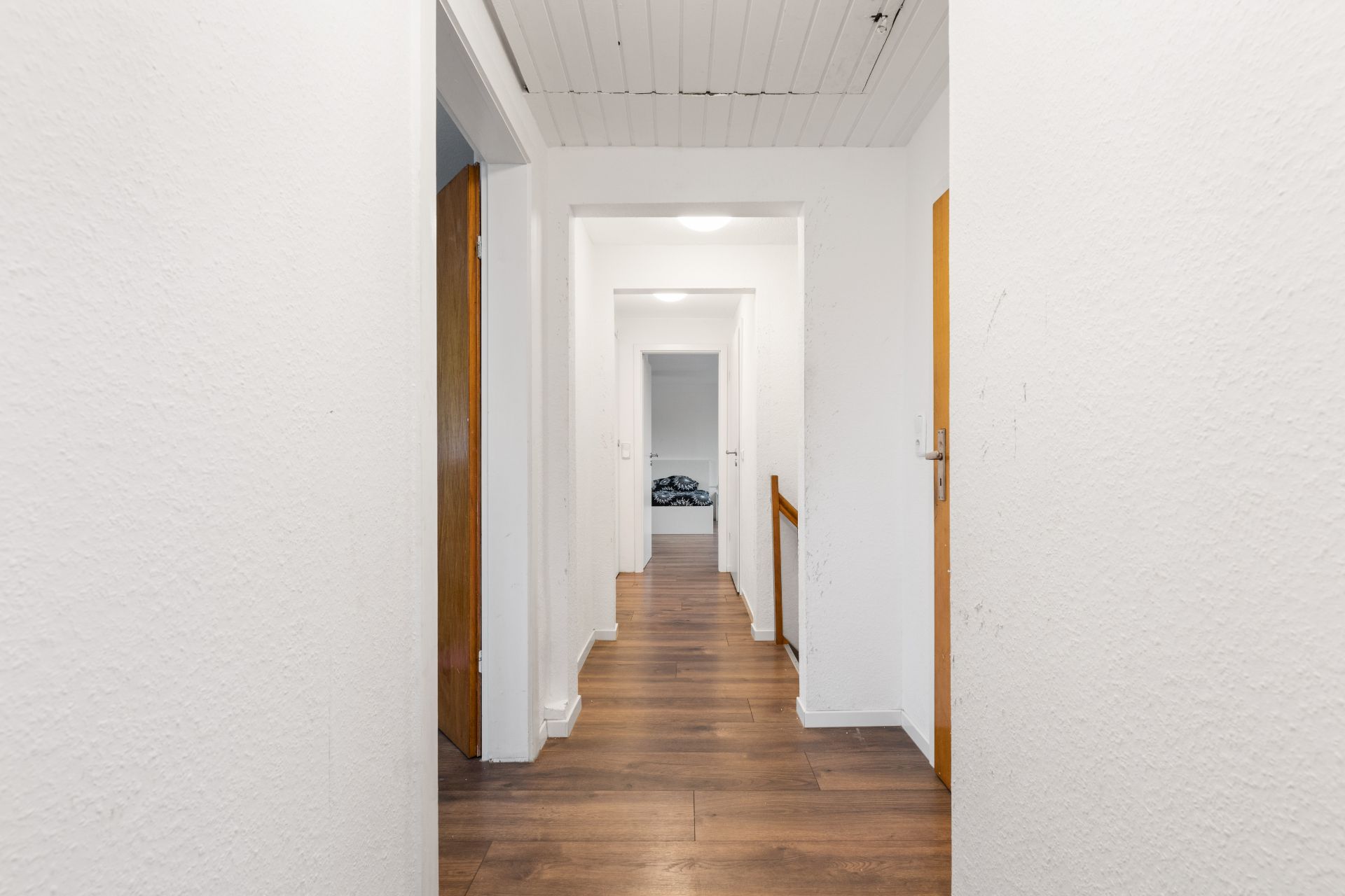 Heller Flur mit Holzboden, mehreren Türen und Sicht auf ein Zimmer am Ende.