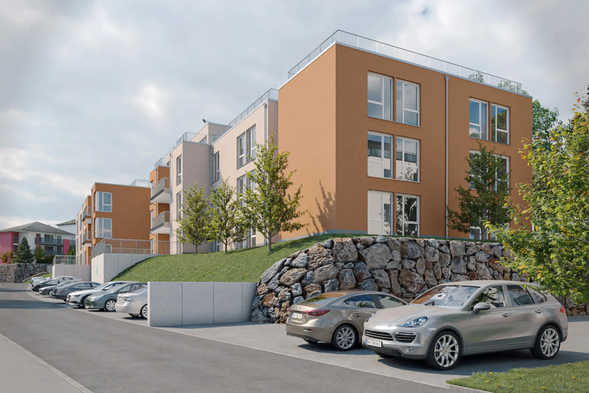 Mehrfamilienhaus mit oranger Fassade, Parkplätzen und Bäumen davor.