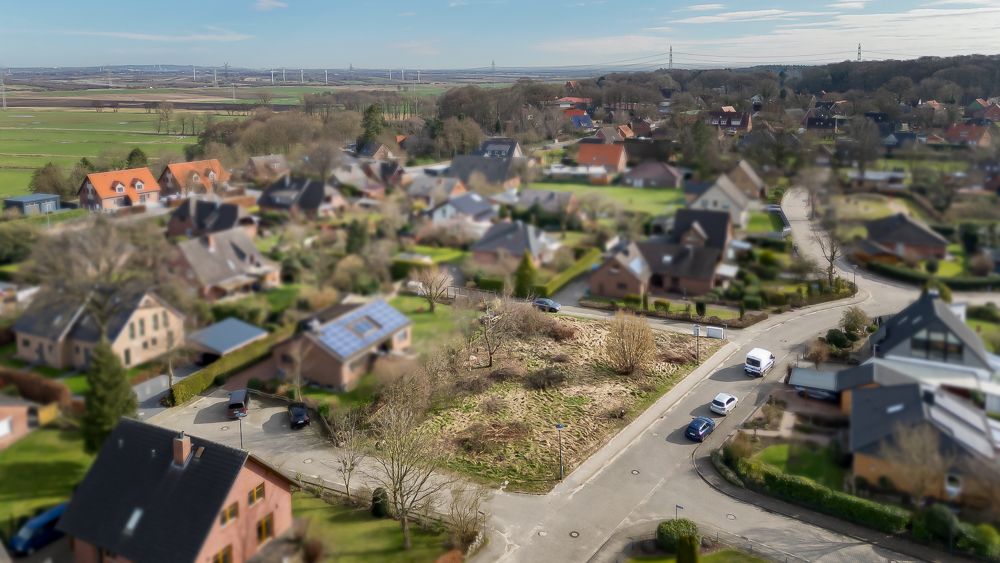 Luftaufnahme eines Wohngebiets mit Einfamilienhäusern und einer freien Baufläche an einer Straßenecke.