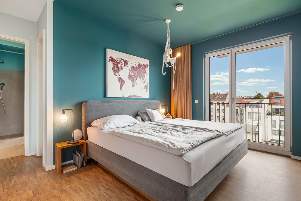 Modernes Schlafzimmer mit grauem Bett, Weltkartenbild, Fenster und Zugang zu Balkon, Holzboden.