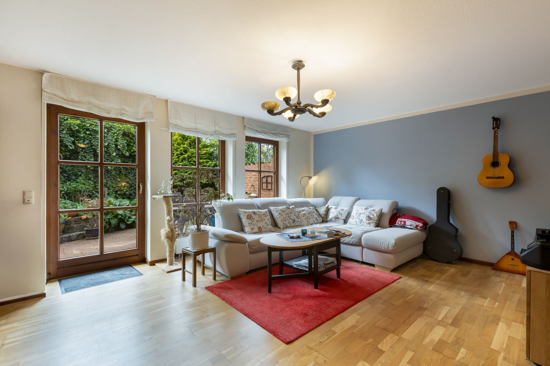 Helles Wohnzimmer mit Ecksofa, rotem Teppich, großen Fenstern und Gitarren an der blauen Wand.