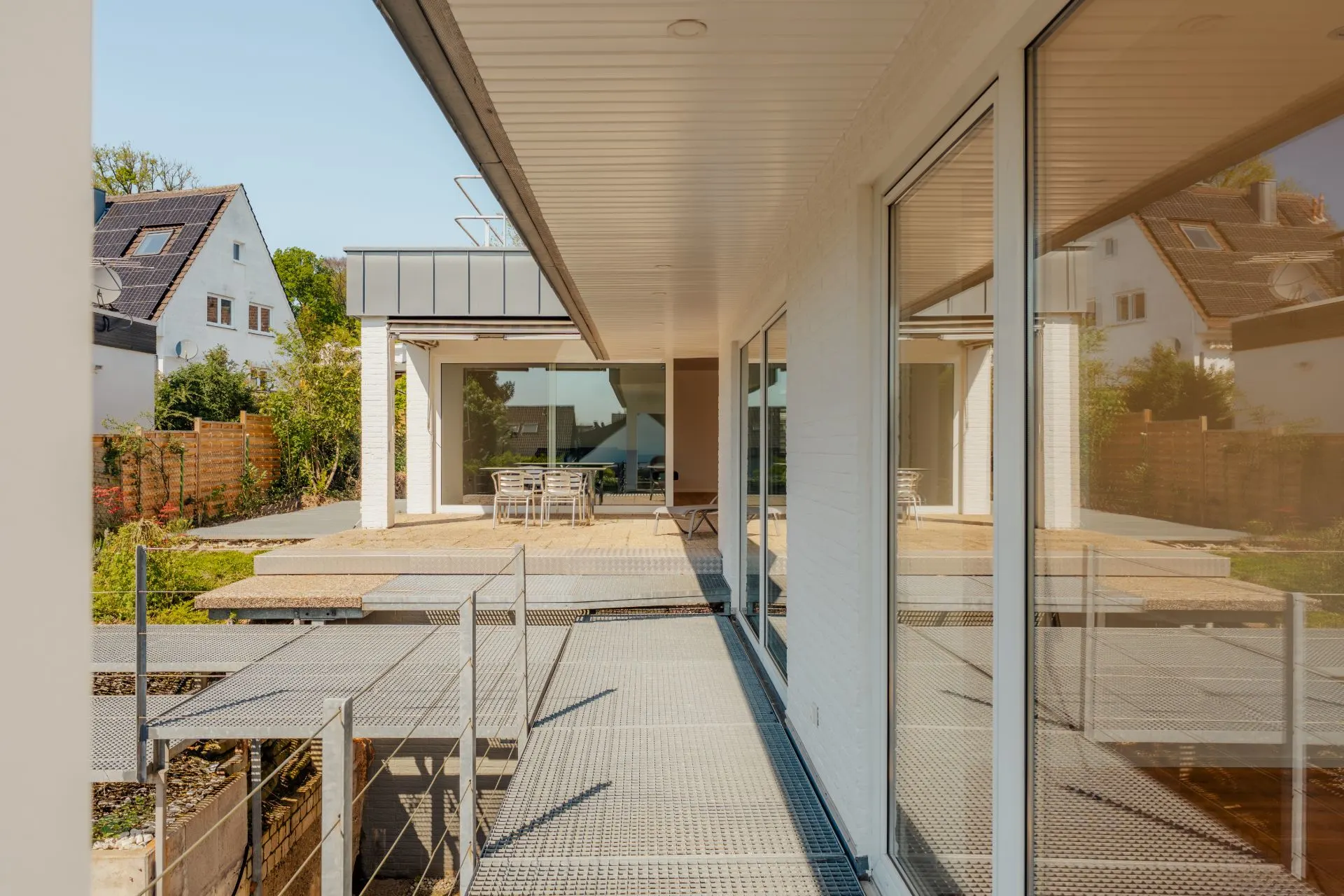 Moderner Wohnhaus-Außenbereich mit Terrasse, Glasfronten und Garten im Hintergrund.