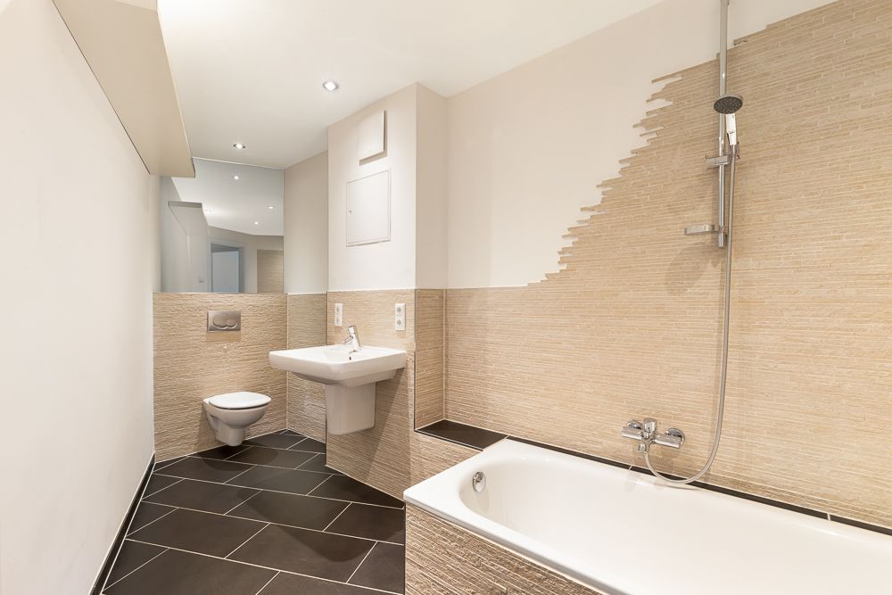 Modernes Badezimmer mit Badewanne, Wandwaschbecken, Toilette und Spiegel.