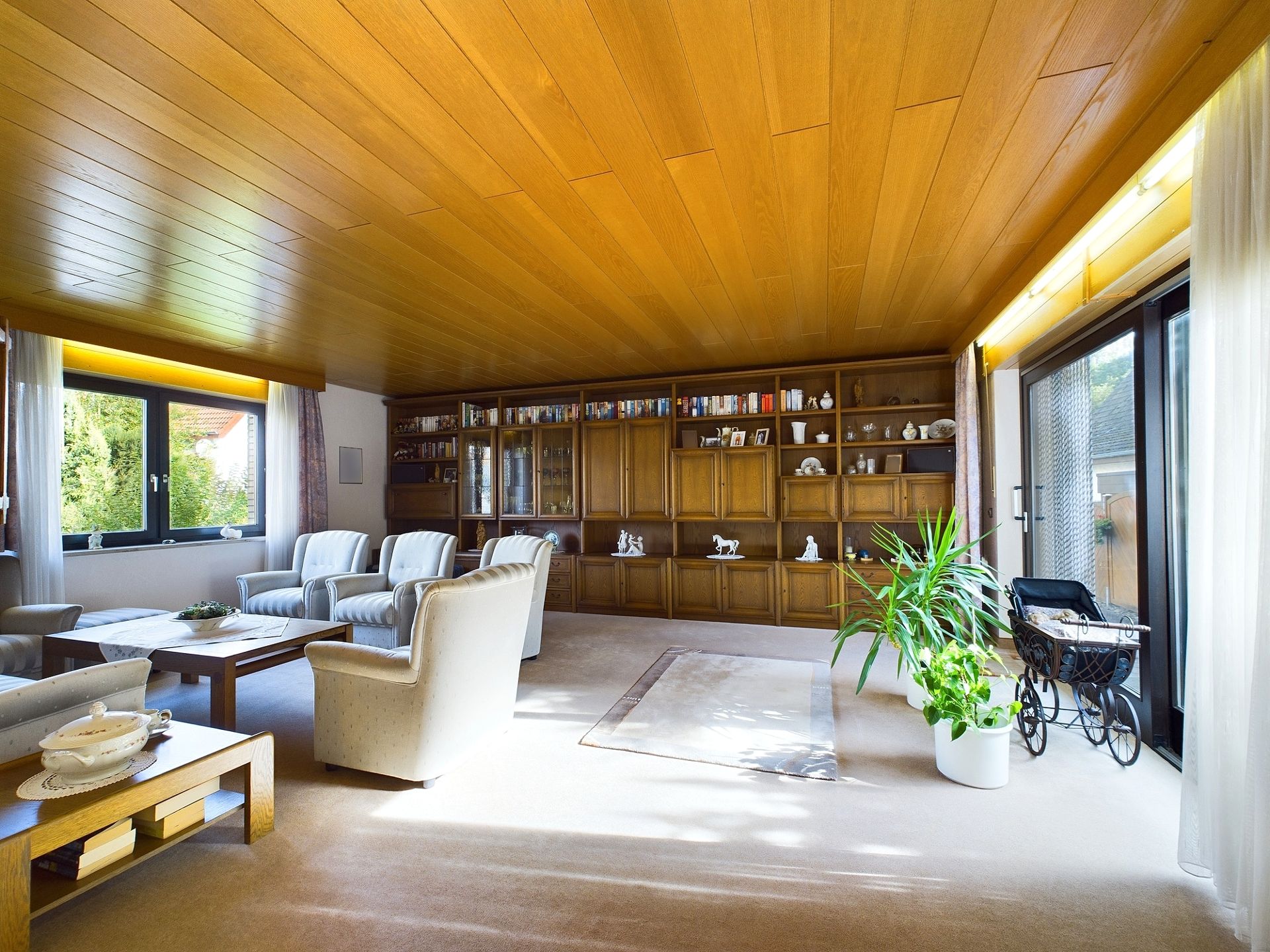 Helles Wohnzimmer mit Holztäfelung, Sofa, Sesseln, Bücherregal und großen Fenstern.