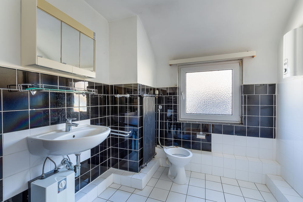 Helles Badezimmer mit Waschbecken, Spiegel, WC und Fenster, schwarze und weiße Fliesen.