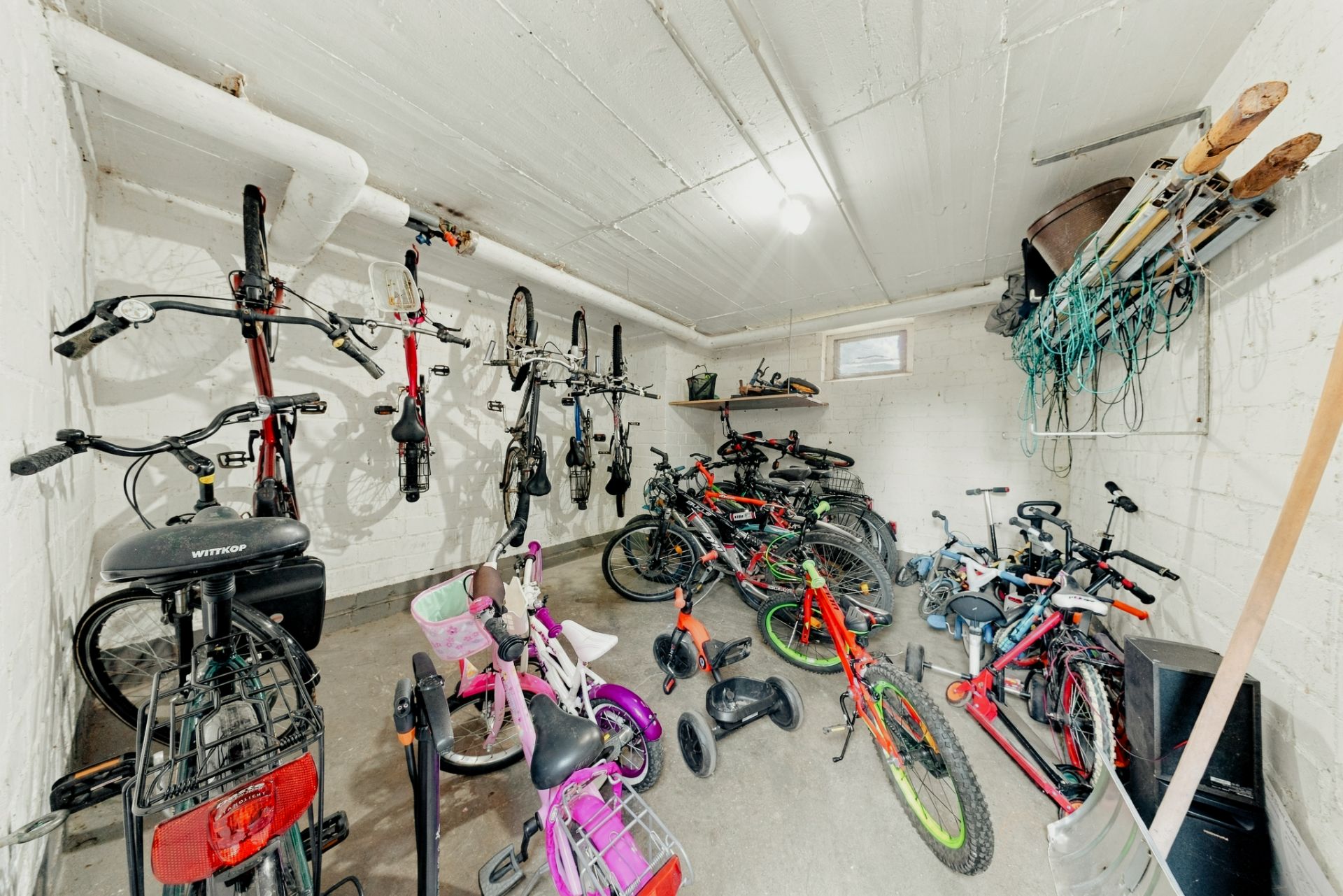 Fahrradraum mit vielen Fahrrädern, Kinderrädern, Rollern und Sportausrüstung an den Wänden.