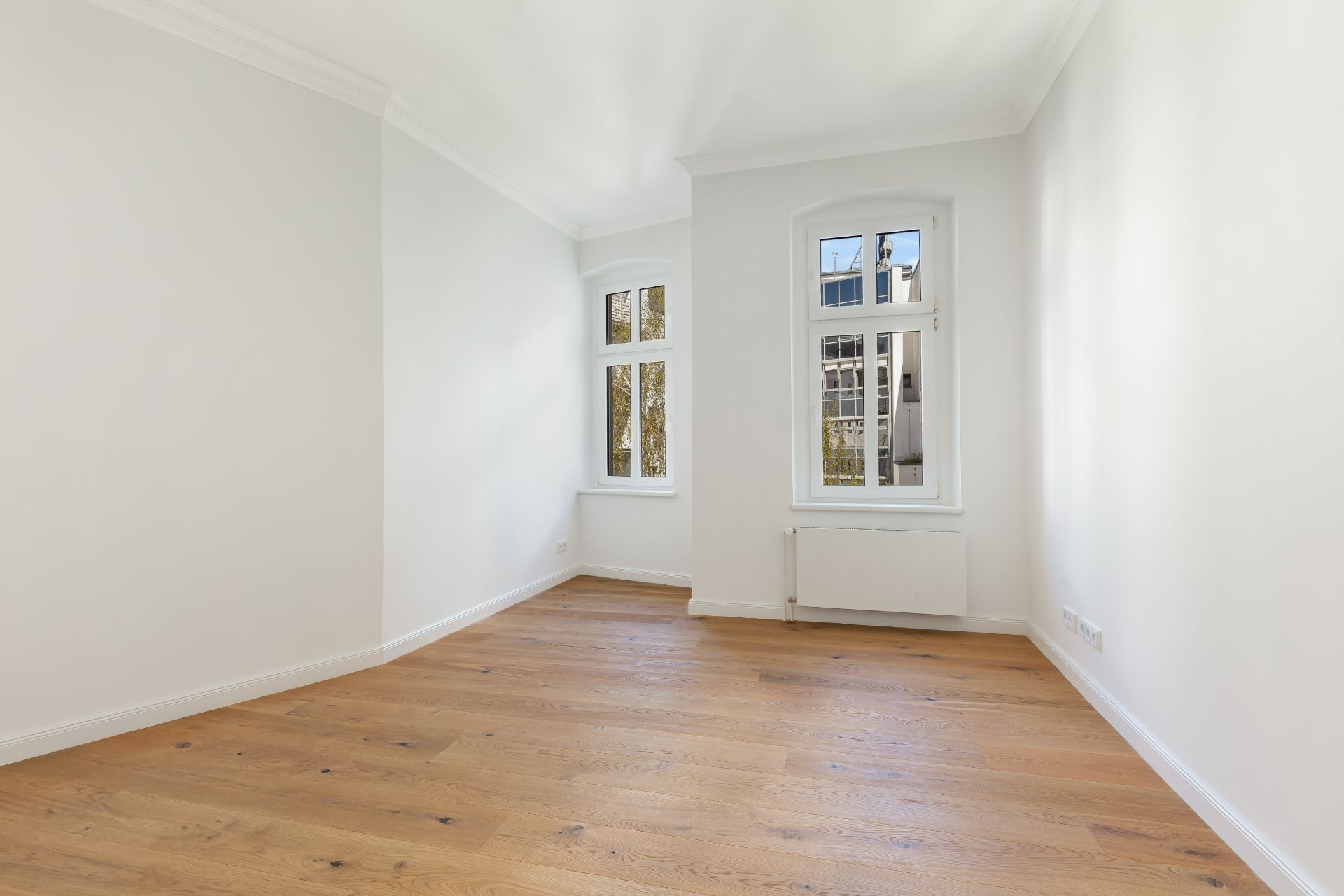 Leerer Raum mit weiß gestrichenen Wänden, Holzboden und zwei Fenstern.