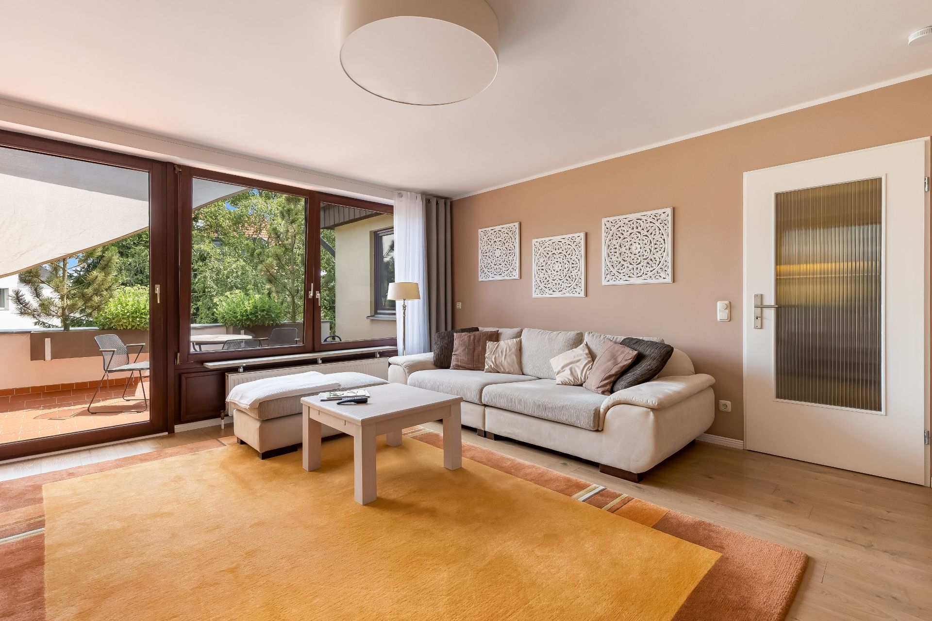 Helles Wohnzimmer mit Sofa, Couchtisch, Teppich und Zugang zu einer Terrasse mit Sitzgelegenheit.