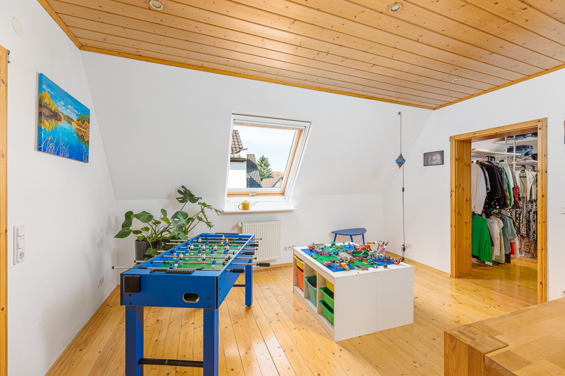 Helles Zimmer mit Dachfenster, Kickertisch, Spieltisch und Zugang zu einem Ankleidezimmer.