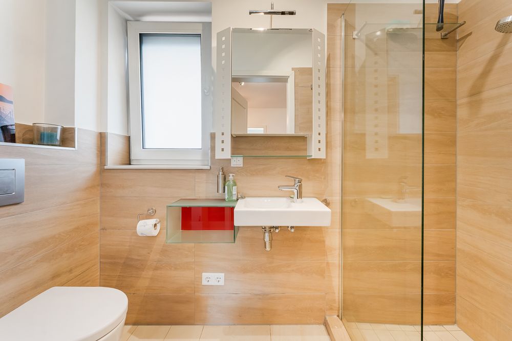 Modernes Badezimmer mit Waschbecken, Spiegel, Dusche und Fenster, Holzoptik an den Wänden.
