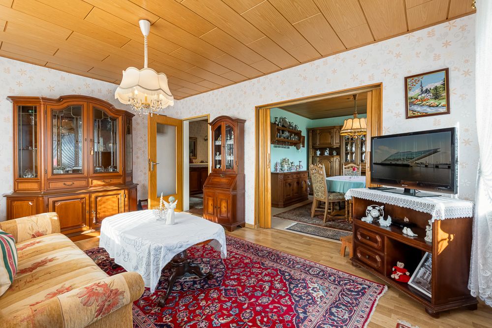 Wohnzimmer mit Holzmöbeln, Sofa, Teppich, Fernseher und Blick ins Esszimmer.