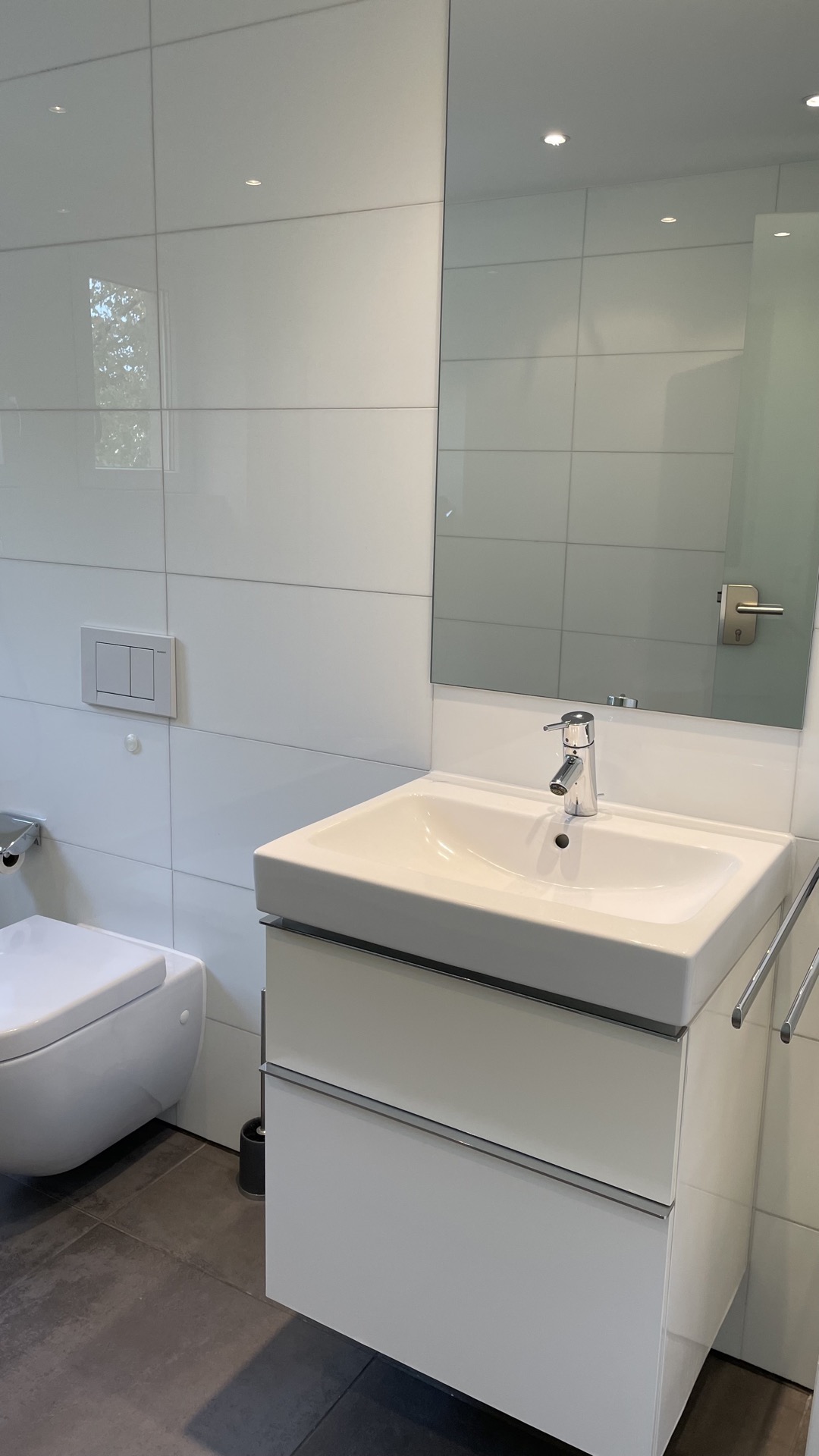 Modernes Badezimmer mit weißem Waschbecken, Spiegel und wandhängender Toilette.
