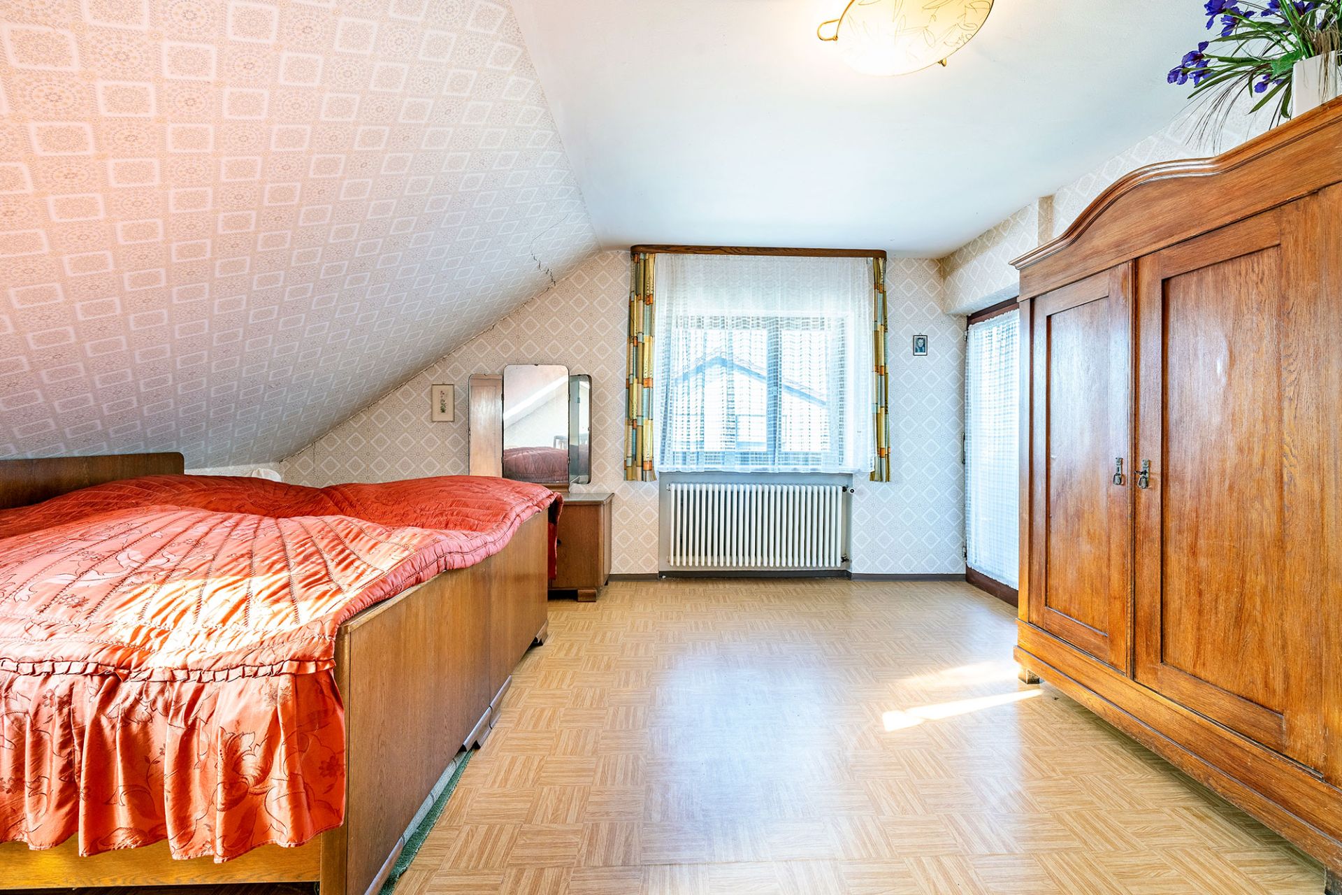 Helles Schlafzimmer mit Dachschräge, Holzschrank, Einzelbett und Fenster mit Vorhängen.