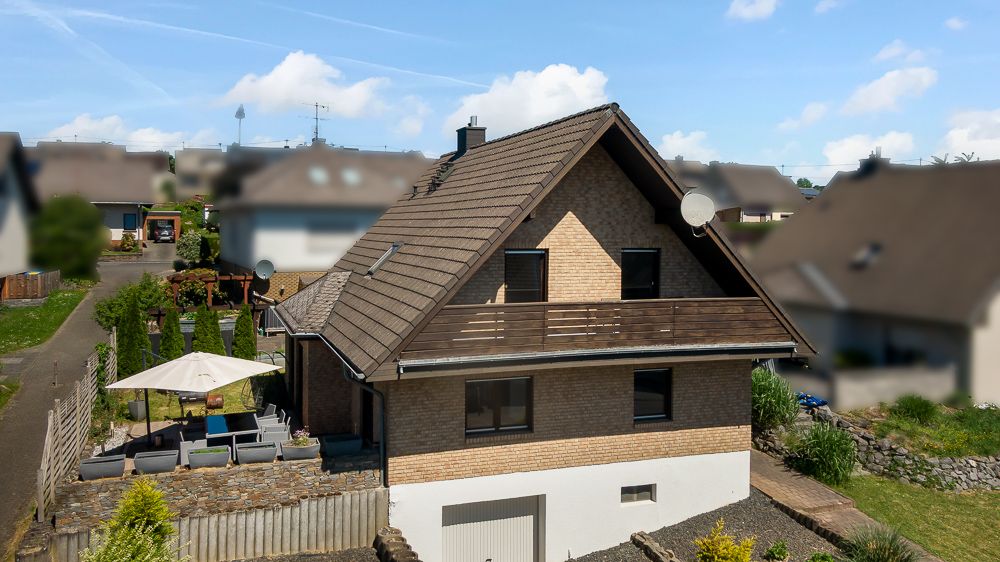 Zweistöckiges Haus mit Satteldach, Terrasse und Gartenmöbeln unter einem Sonnenschirm.