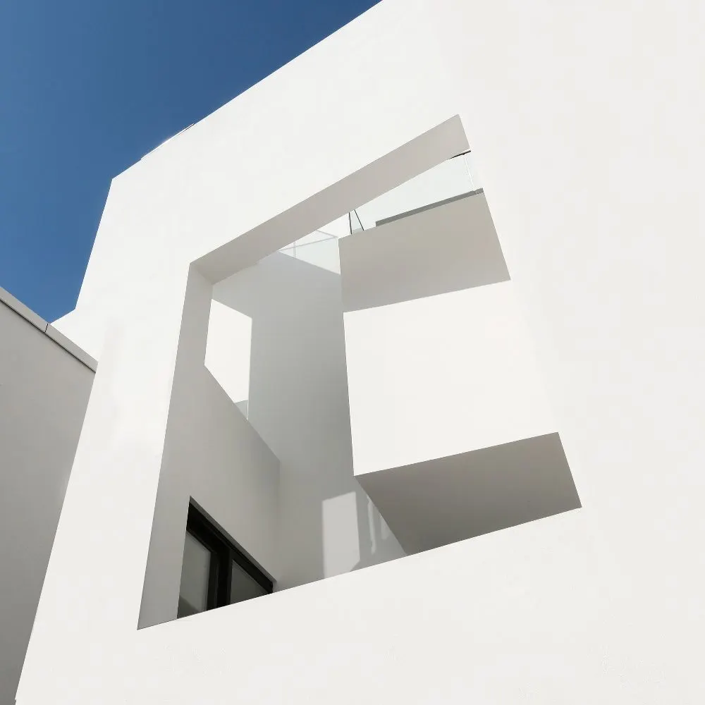 Moderne weiße Fassade mit geometrischen Formen vor blauem Himmel.