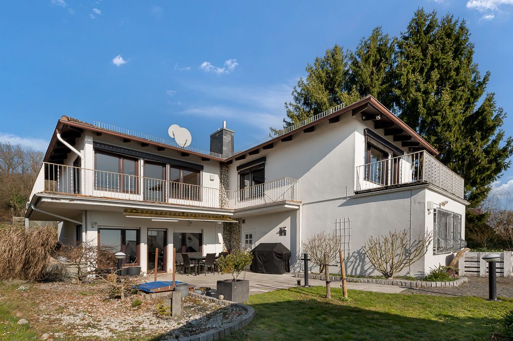 Zweistöckiges Wohnhaus mit Balkonen, Terrasse und Garten unter blauem Himmel.
