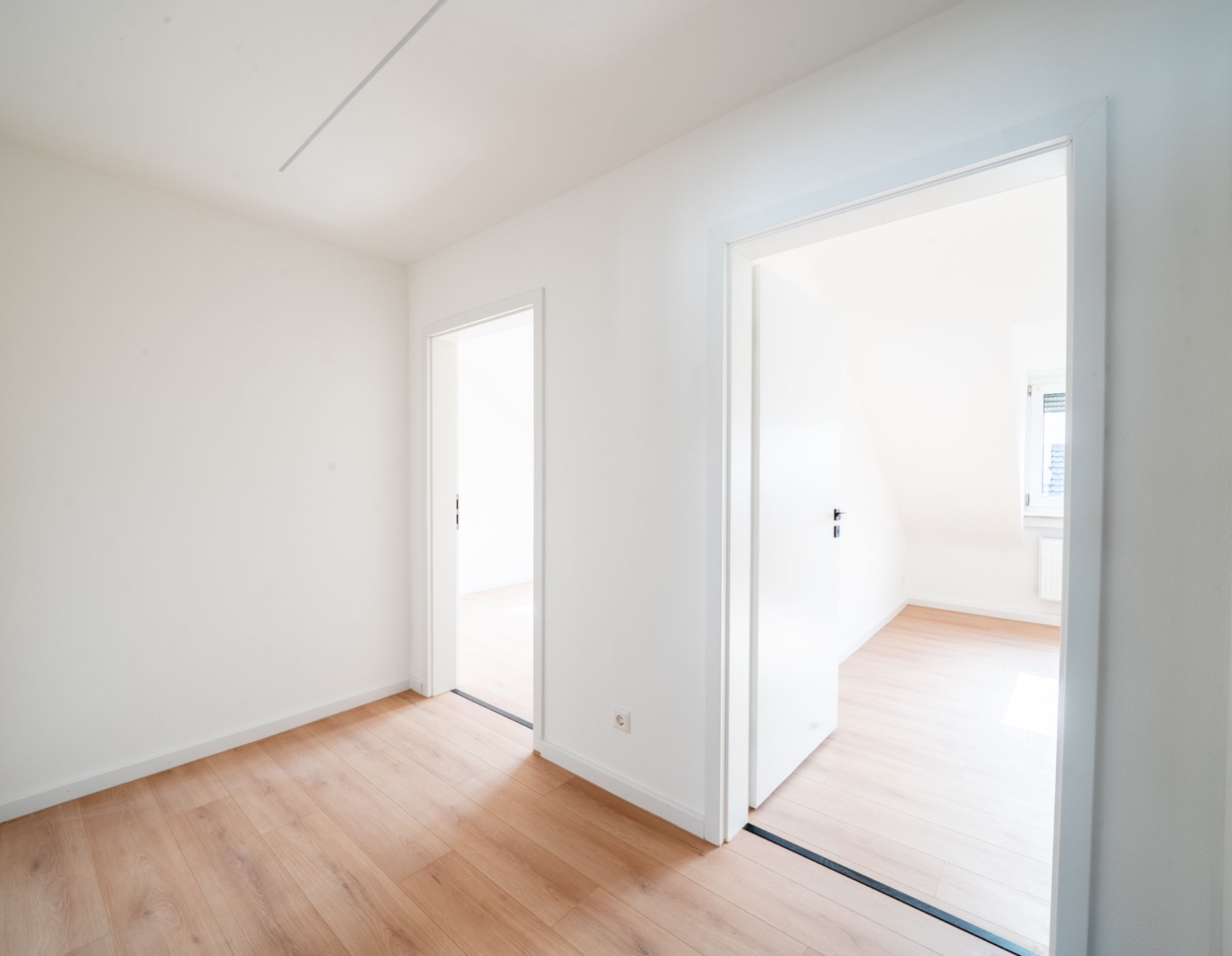 Heller Flur mit zwei offenen Türen und Holzfußboden in einer Wohnung.