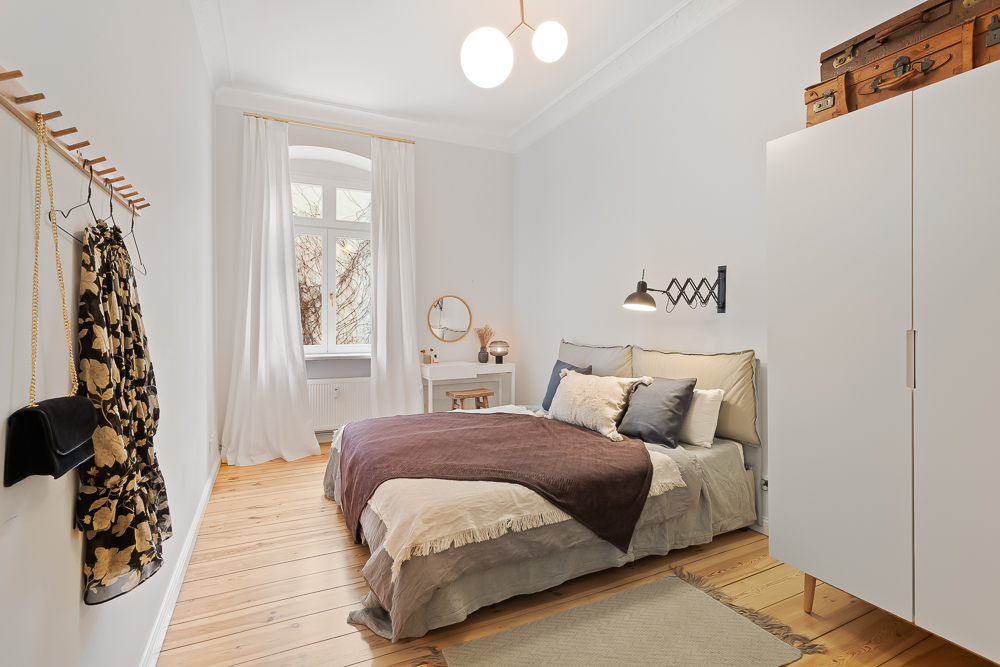 Helles Schlafzimmer mit Doppelbett, weißem Schrank, großem Fenster und Holzfußboden.