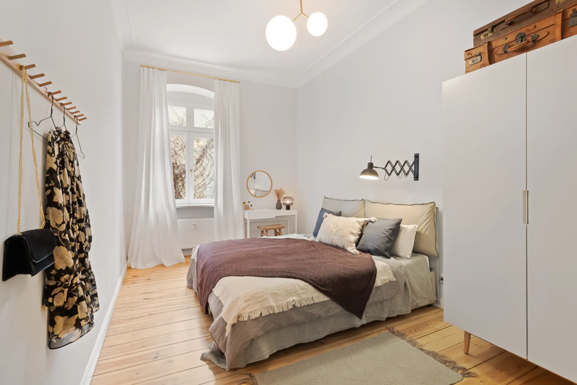 Helles Schlafzimmer mit Doppelbett, weißem Schrank, großem Fenster und Holzfußboden.