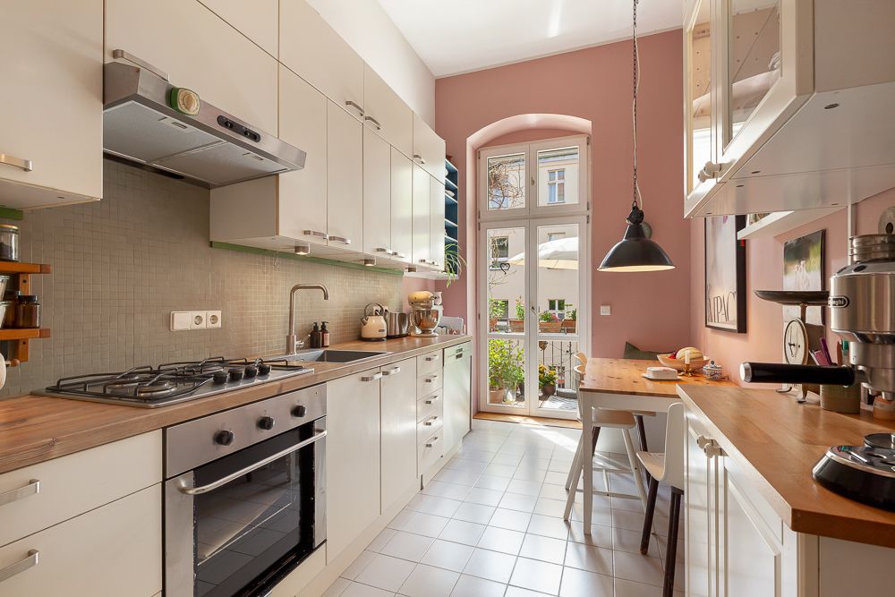Helle Küche mit weißen Schränken, Holzarbeitsplatten und Esstisch vor Tür zum Balkon.