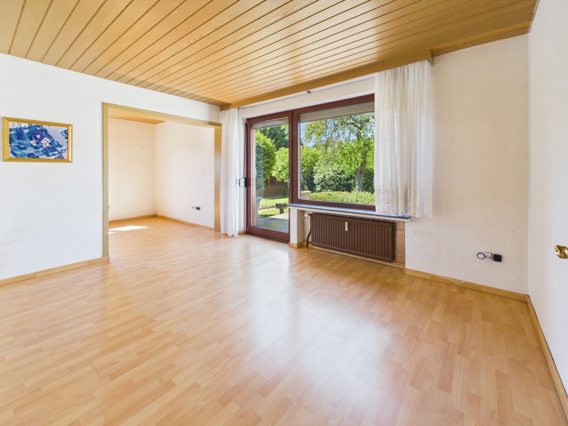 Helles Wohnzimmer mit Holzdecke, großem Fenster und Blick in den Garten.
