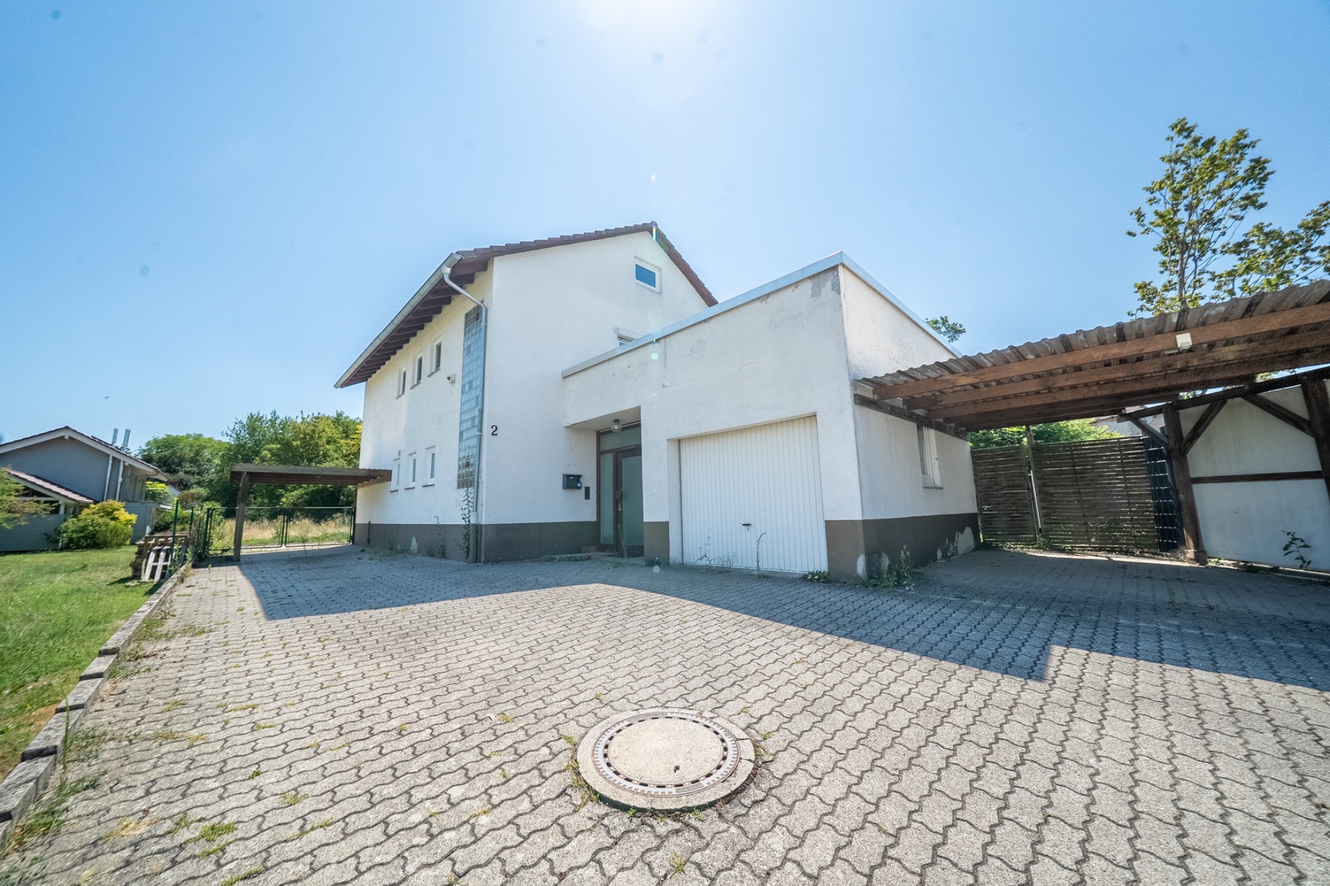 Zweistöckiges Wohnhaus mit Garage, Carport und gepflastertem Vorhof bei sonnigem Wetter.