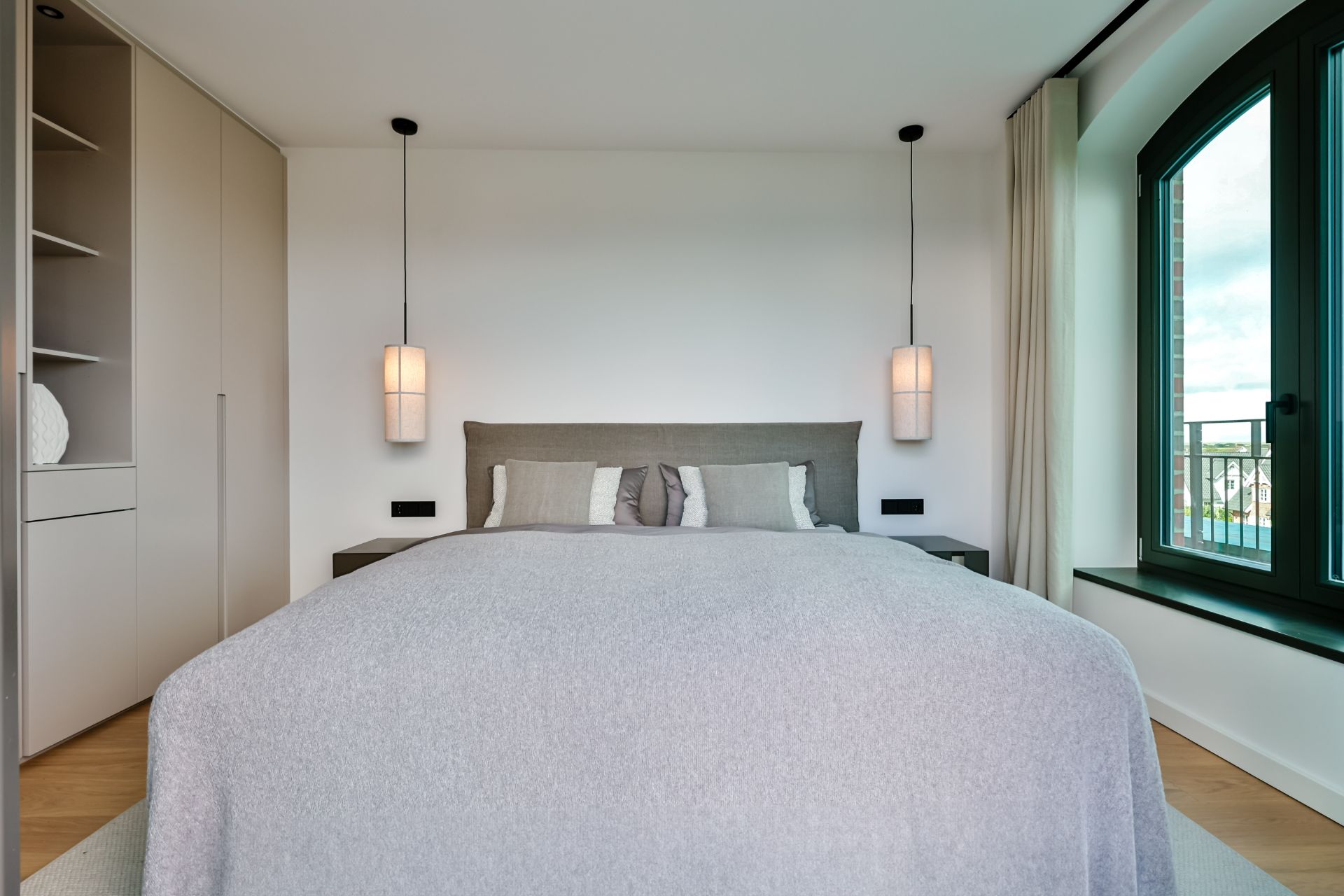 Modernes Schlafzimmer mit Doppelbett, zwei Hängelampen und großem Fenster.