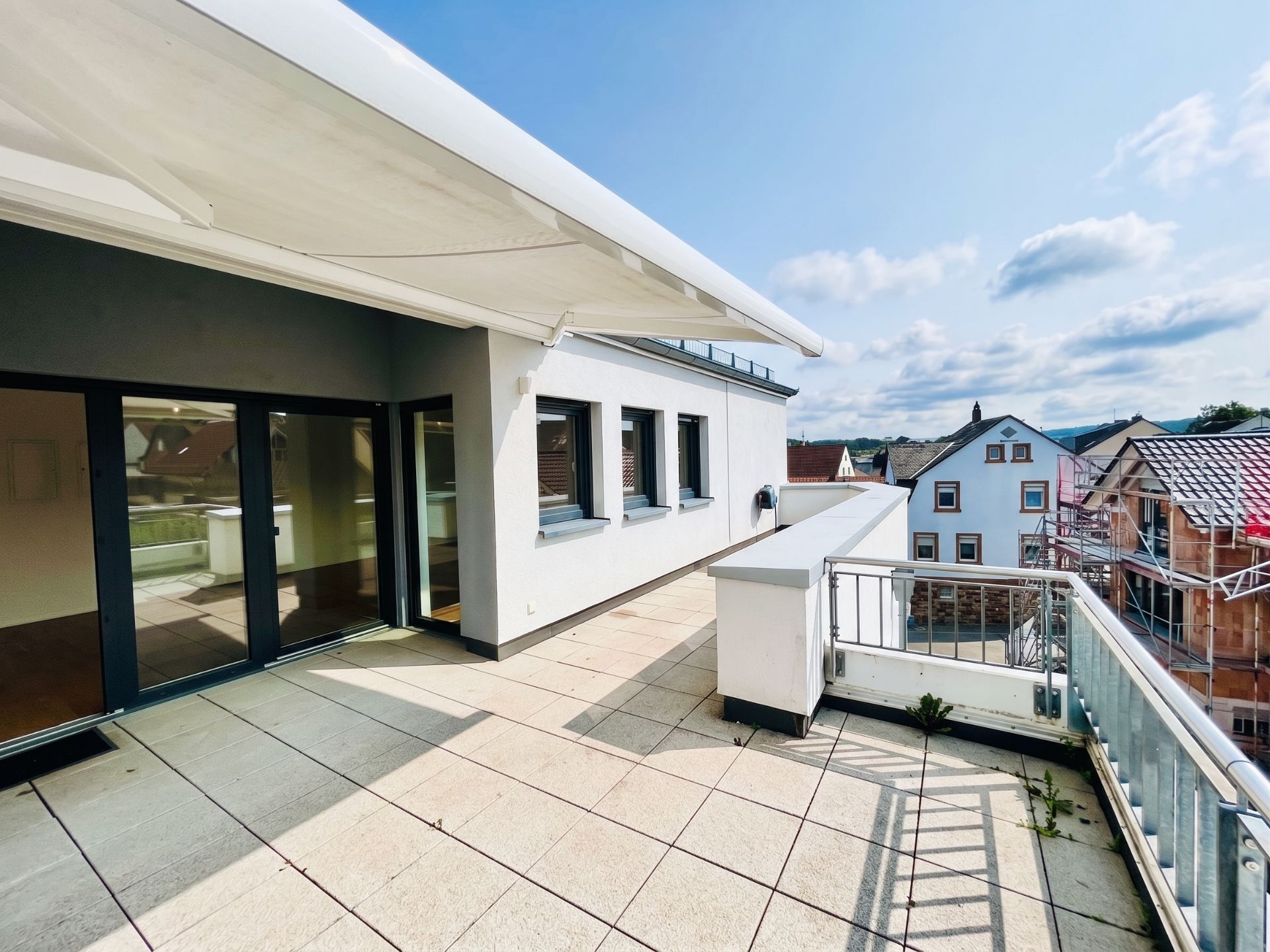 Große Dachterrasse mit Überdachung und Geländer, Zugang durch Glastüren, Blick auf Nachbarhäuser.