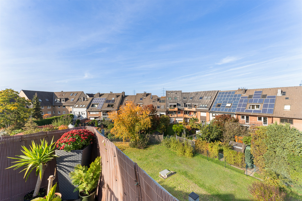 Blick von einem Balkon auf einen grünen Garten und Reihenhäuser mit Solarpanelen auf den Dächern.
