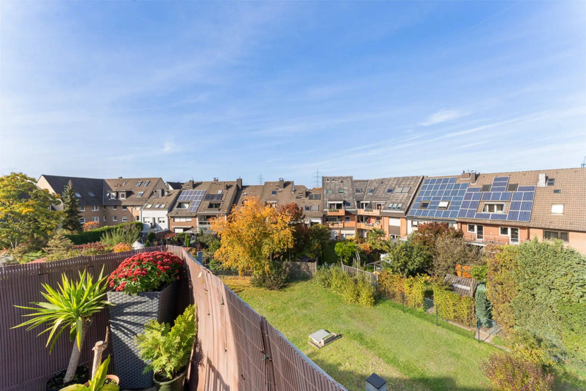 Blick von einem Balkon auf einen grünen Garten und Reihenhäuser mit Solarpanelen auf den Dächern.