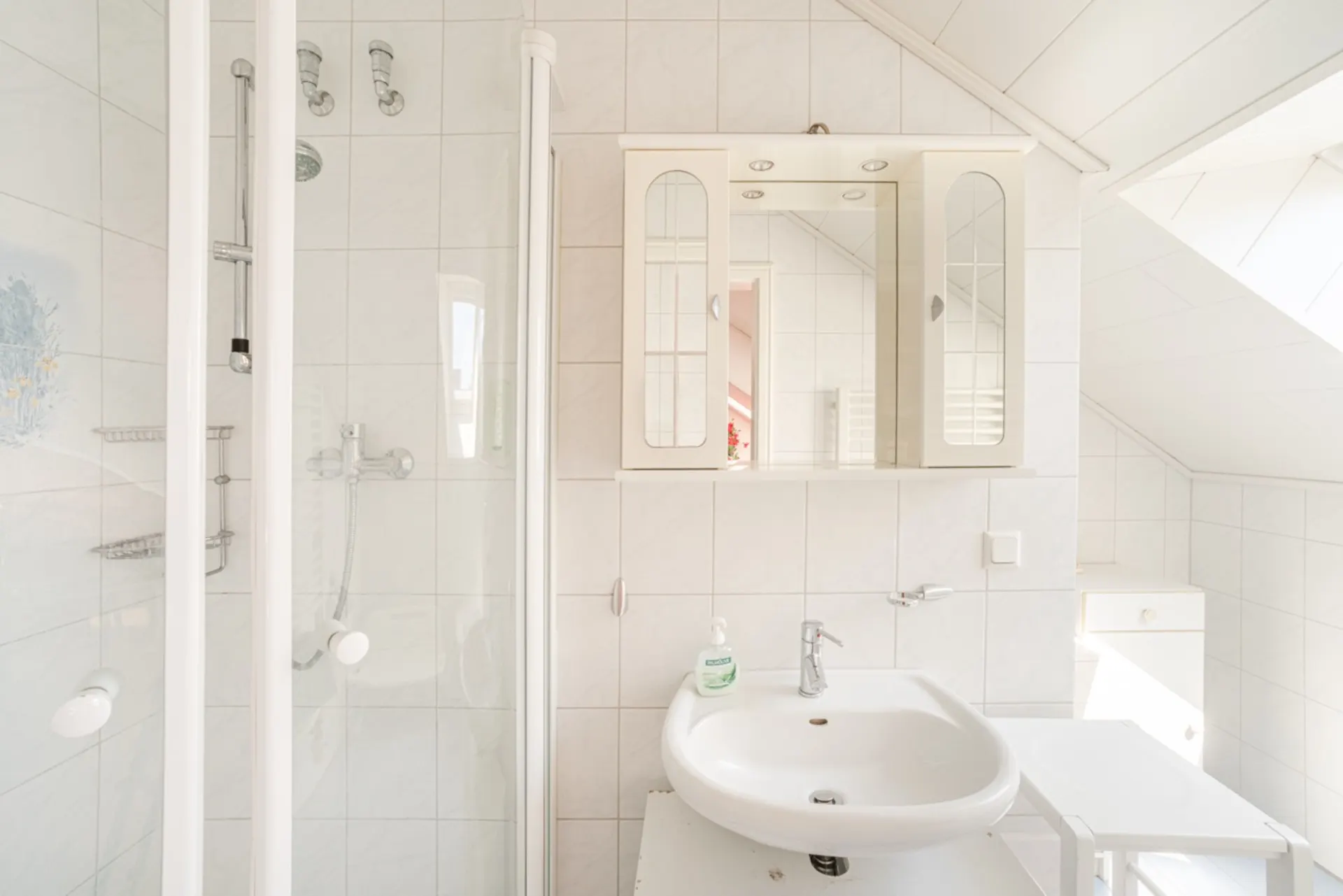 Helles Badezimmer mit Dusche, Waschbecken, Spiegel und weiß gefliesten Wänden.