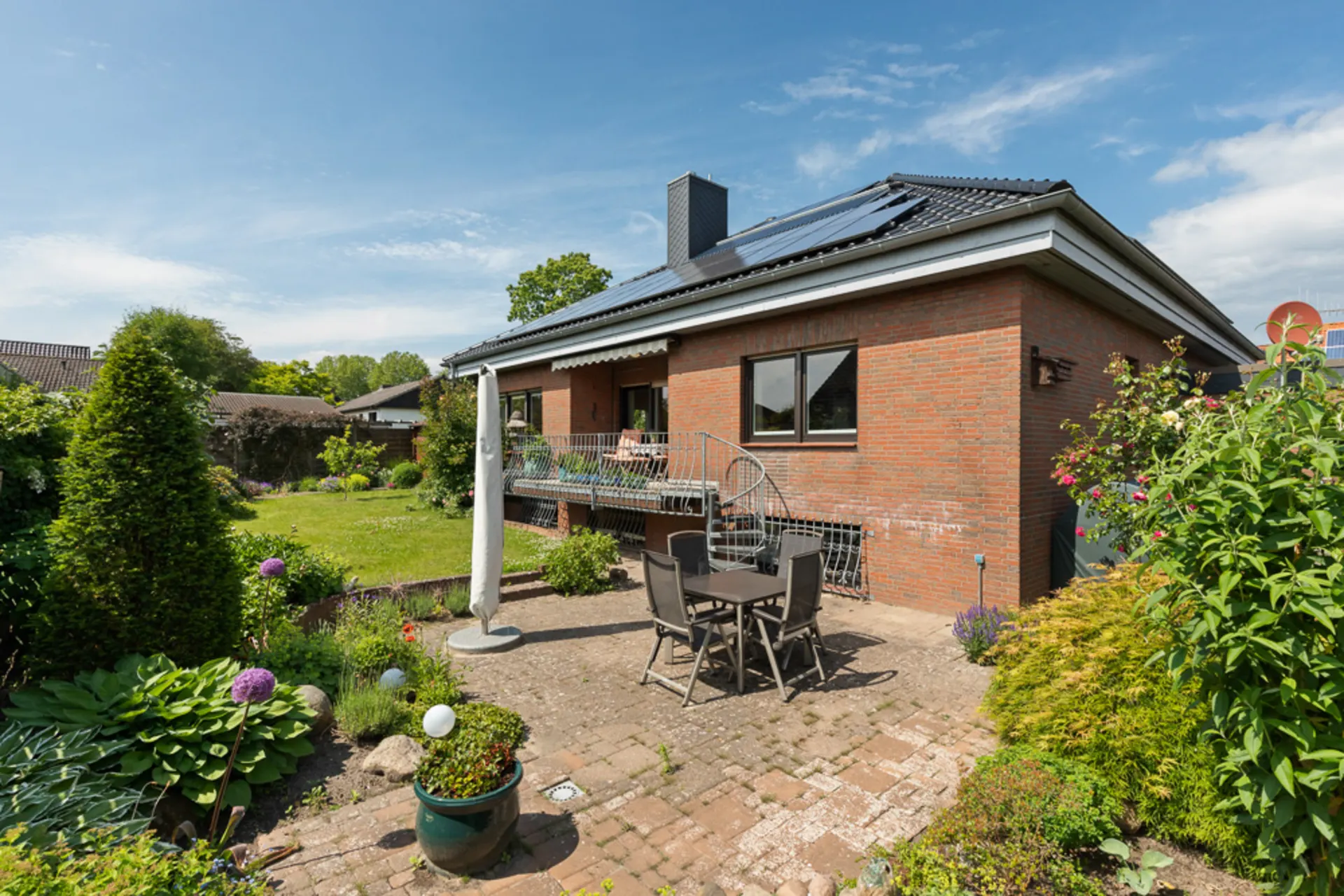 Backsteinwohnhaus mit Terrasse, Gartenmöbeln und gepflegtem Garten bei sonnigem Wetter.