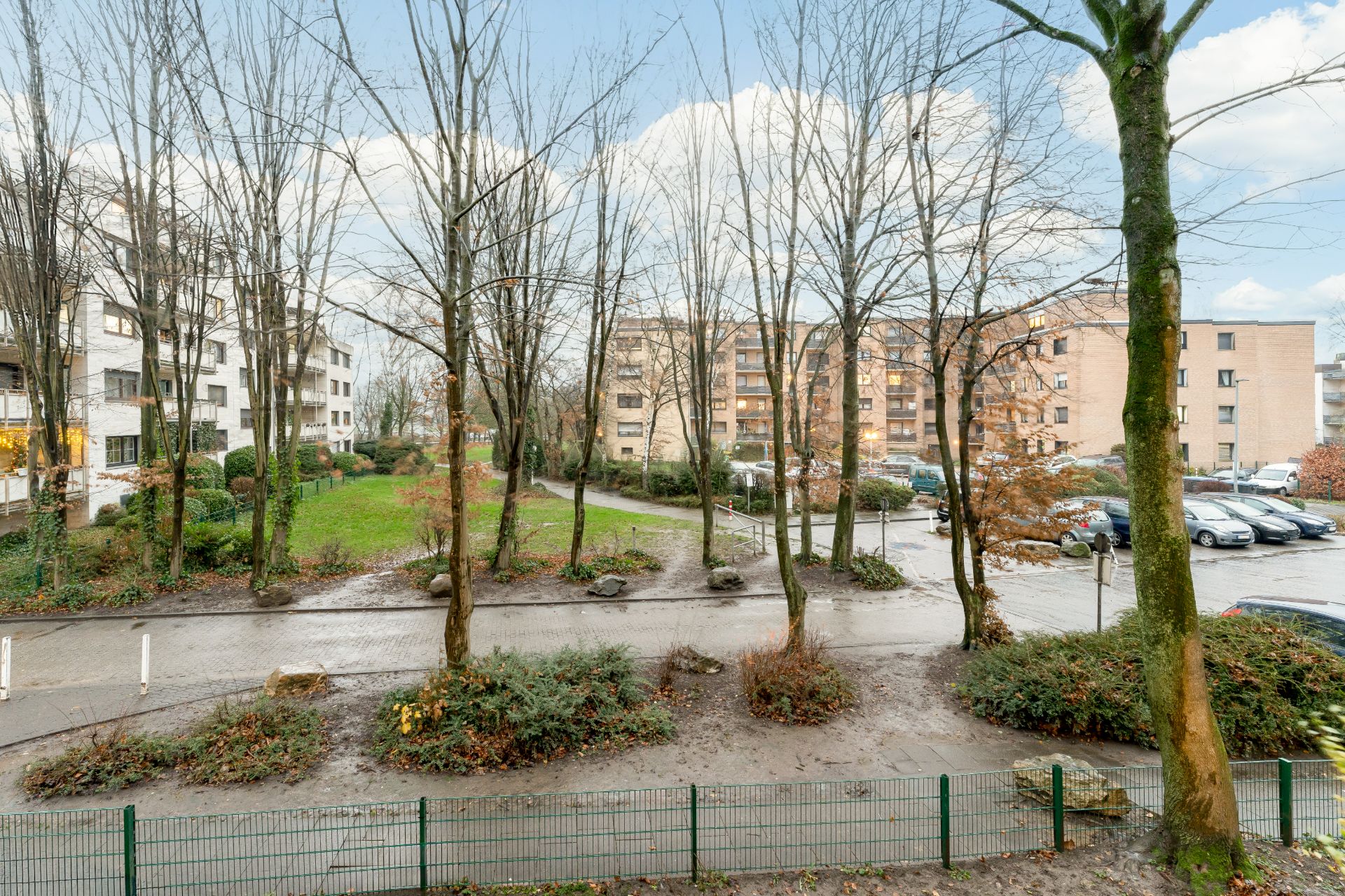 Blick auf Wohnhäuser, Bäume, Wege und geparkte Autos an einem regnerischen Tag.