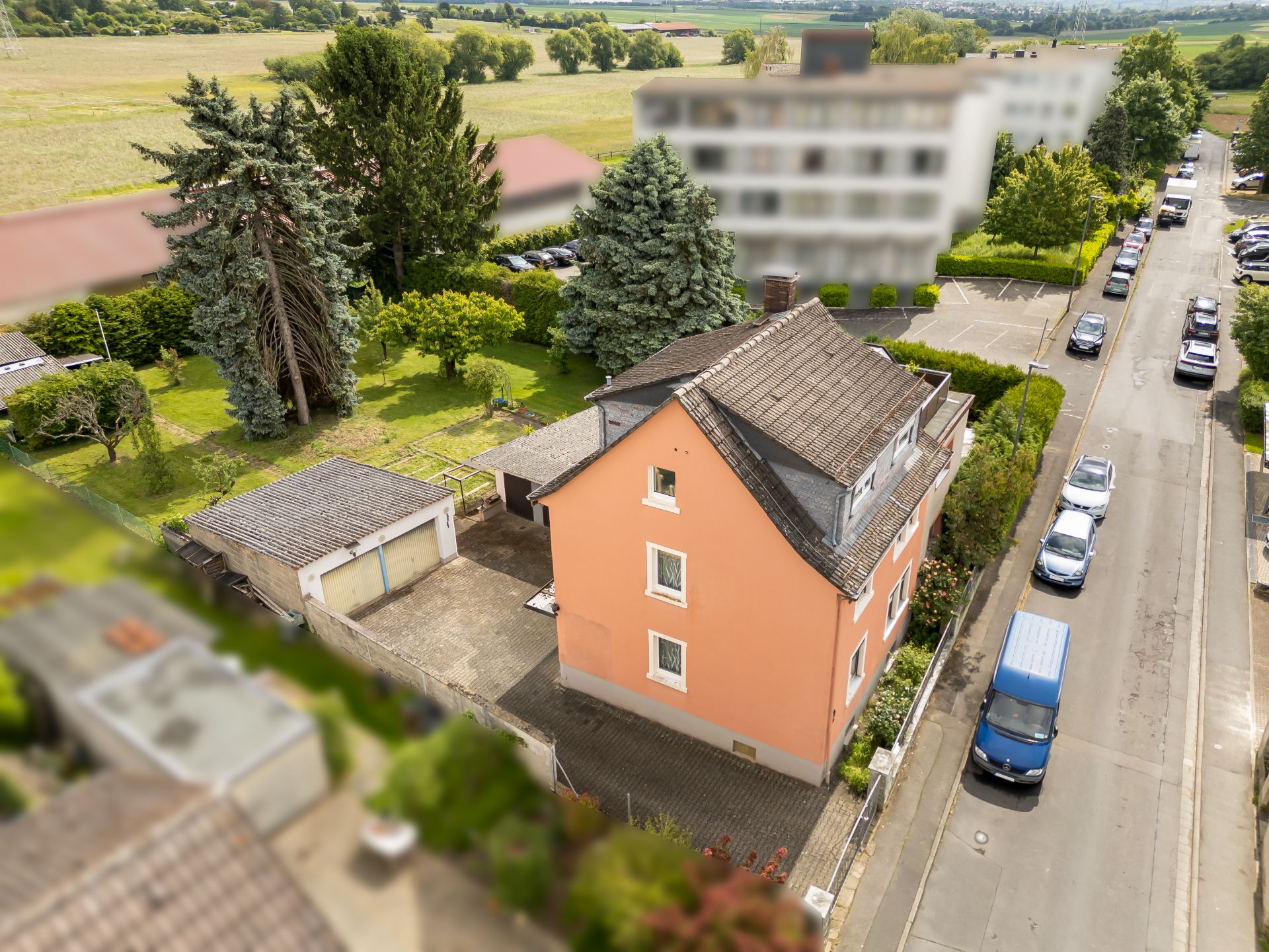 Lachsfarbenes Einfamilienhaus mit Hof, Garage und Garten an einer ruhigen Straße.