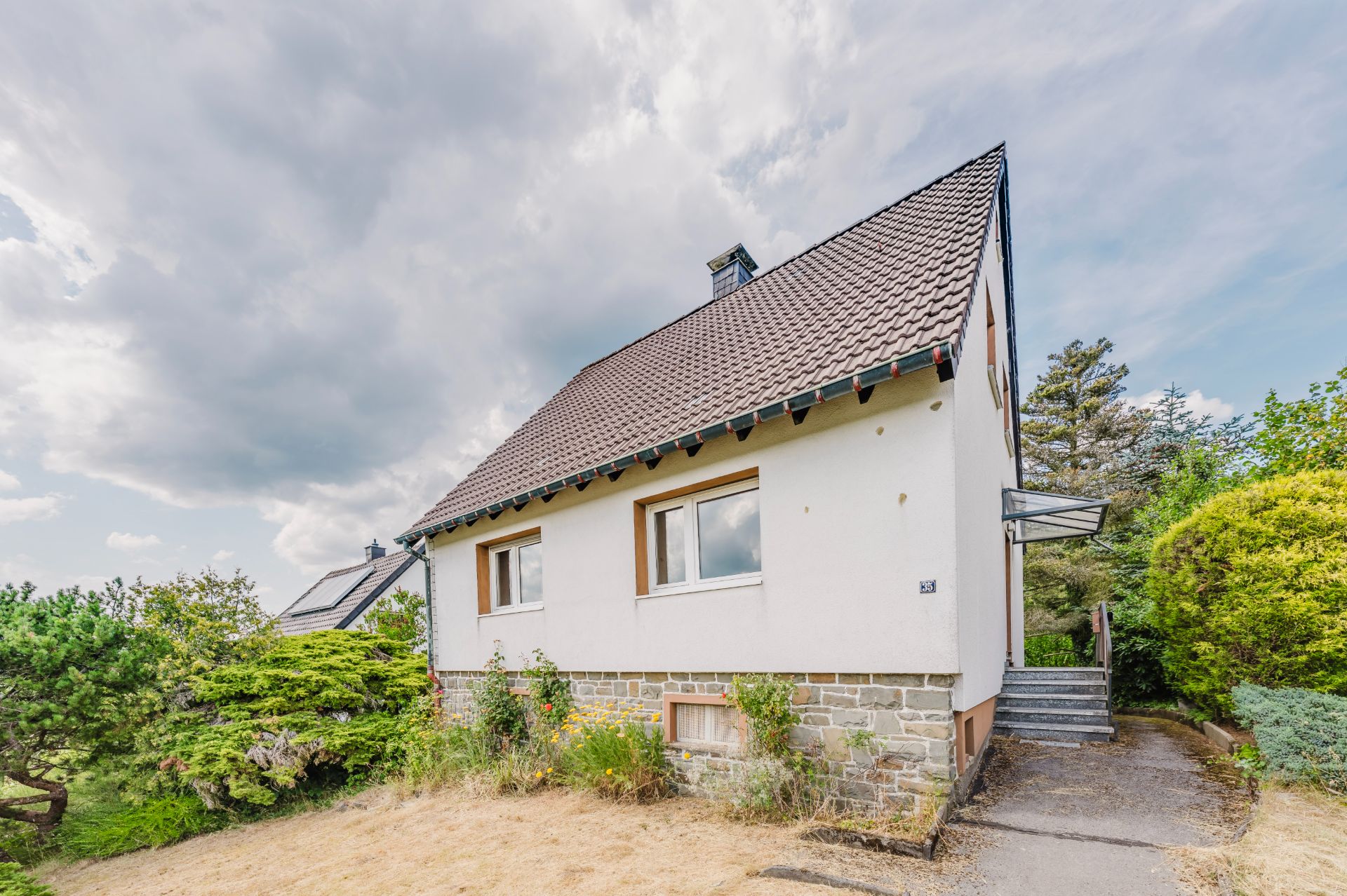 Einfamilienhaus mit Satteldach, weißen Wänden und kleinem Garten, Treppe am Seiteneingang.