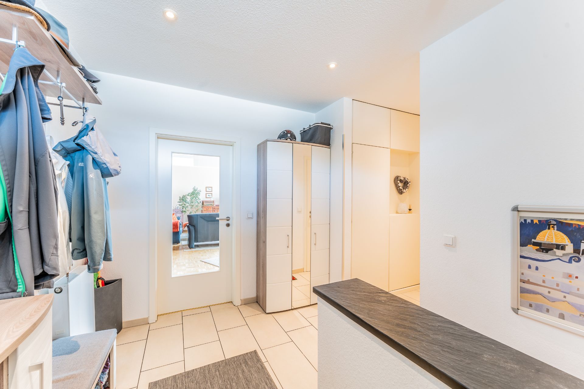 Heller Flur mit Garderobe, weißen Schränken und einer Glastür zum Wohnzimmer.
