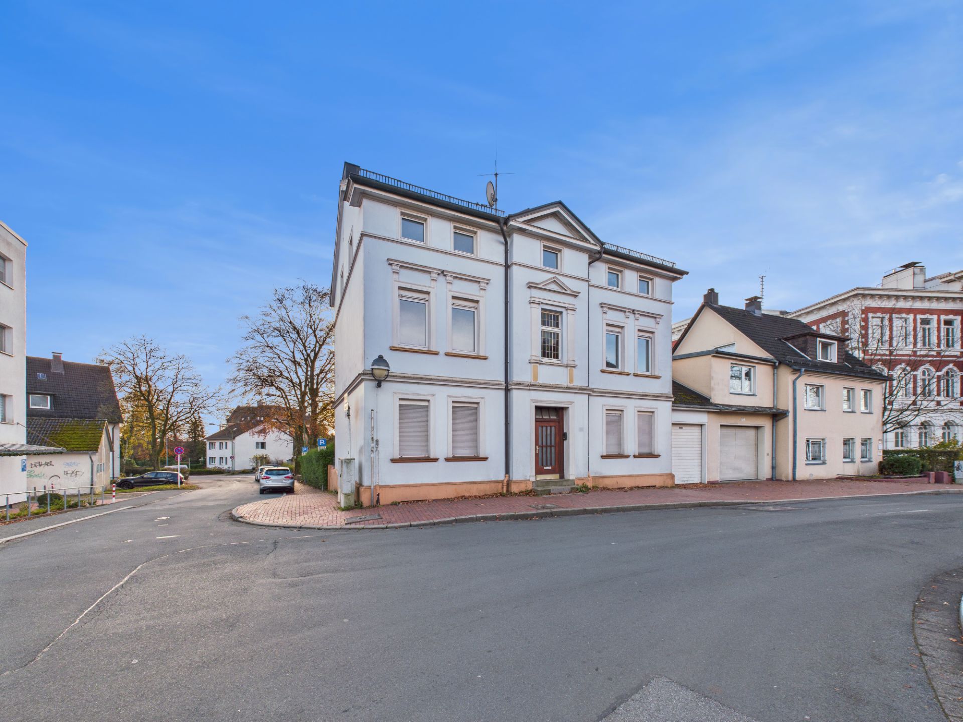 Eckhaus mit weißer Fassade und mehreren Fenstern, an einer ruhigen Straße gelegen.