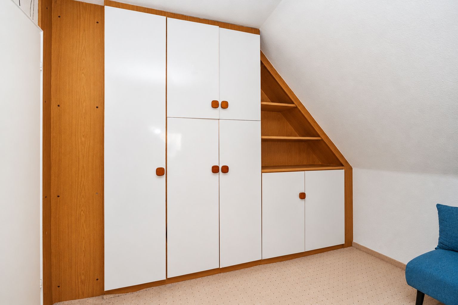Einbauschrank mit weißen Türen und offenen Regalen unter einer abgeschrägten Zimmerdecke.